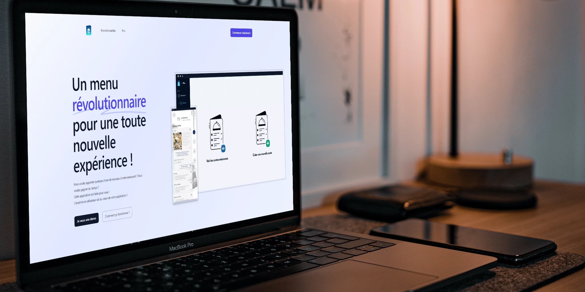 A laptop displaying a website in French promoting an innovative digital menu, with a smartphone and closed notebook on a modern workspace desk.