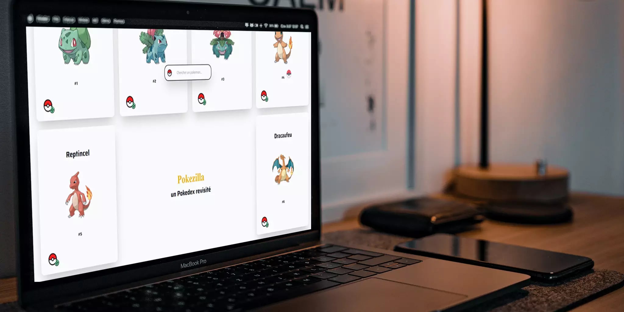 Laptop displaying illustrated creatures, smartphone, and wooden object on desk in casual workspace setting