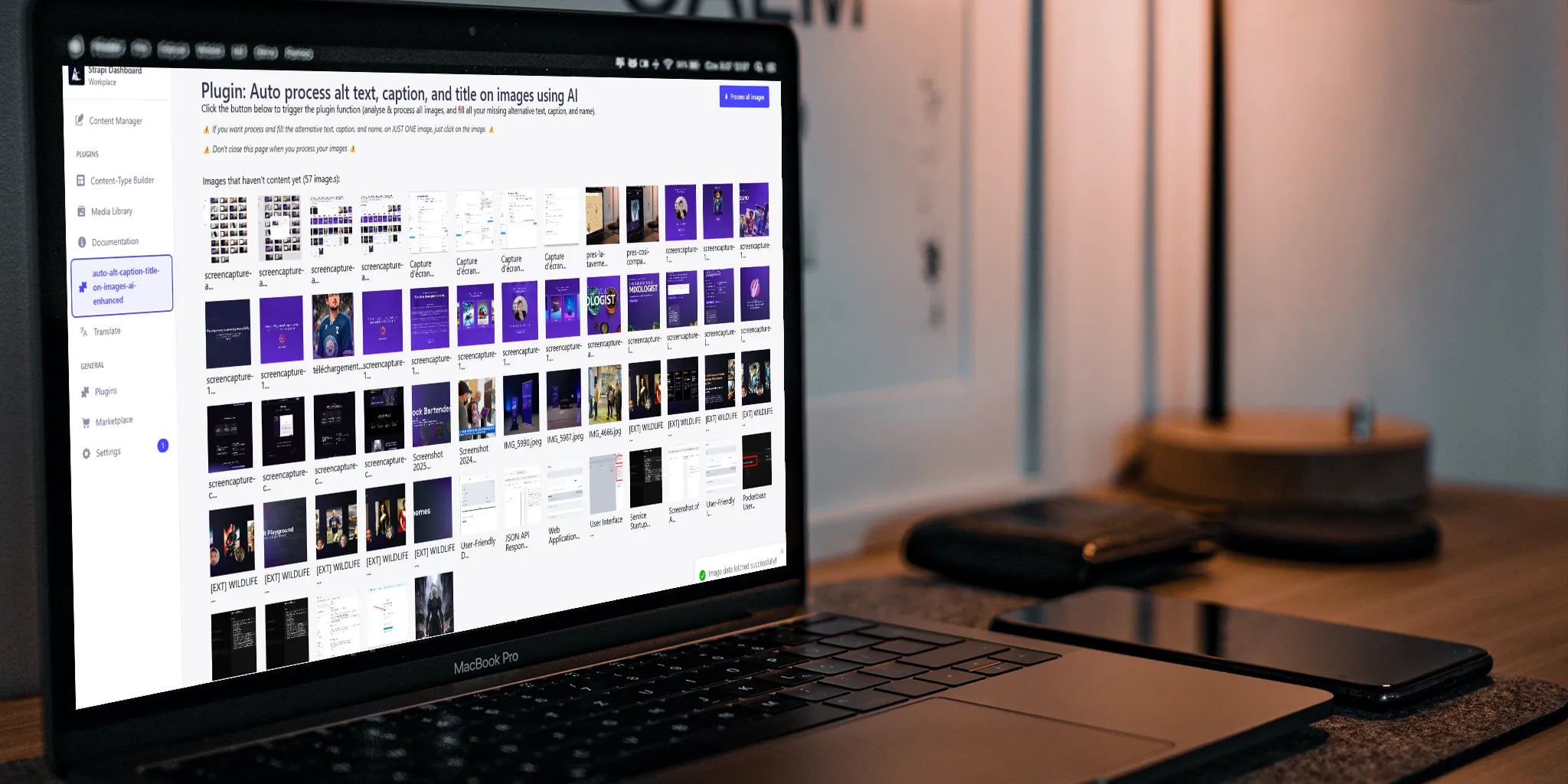 A MacBook Pro on a wooden desk displaying a digital interface for AI-powered image alt text and caption processing, with two smartphones and ambient lighting in a modern workspace.