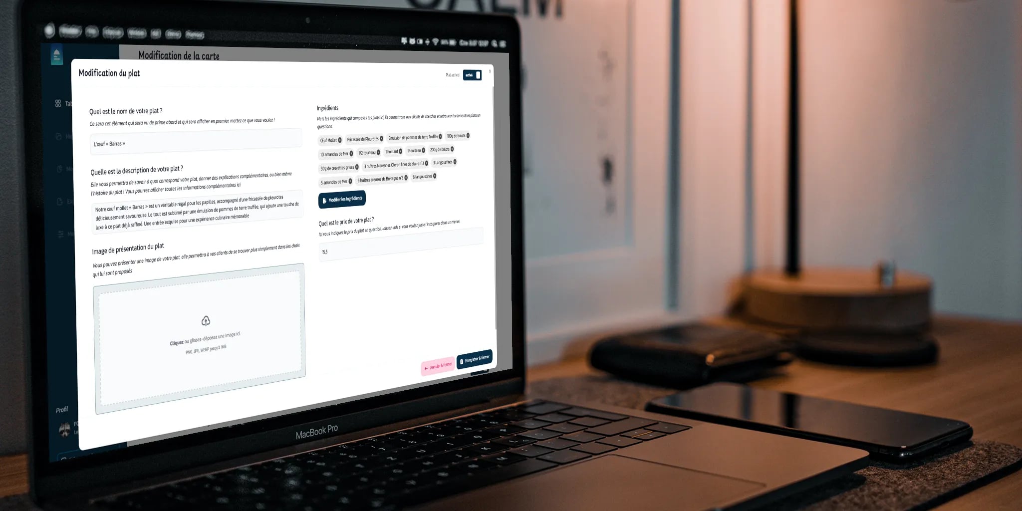 Open laptop displaying a French food dish editing form, with a smartphone and notebook on the table