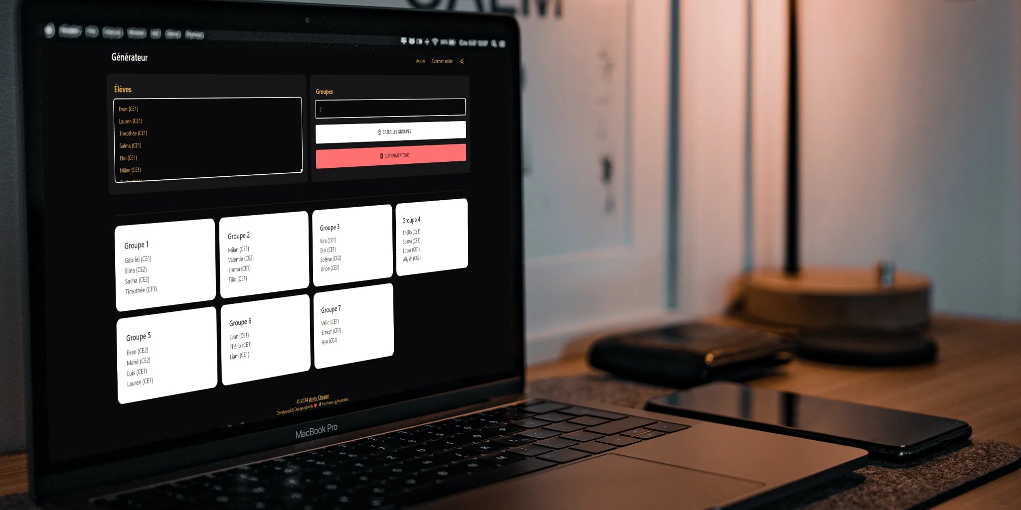 Laptop displaying group generation tool, smartphone and lamp on desk in home office setting