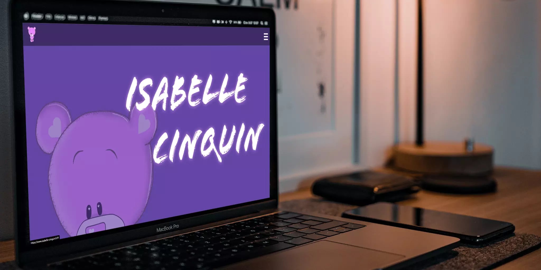 Cartoonish elephant illustration on laptop screen with 'ISABELLE CLINQUIN' text, smartphone and notepad on wooden desk